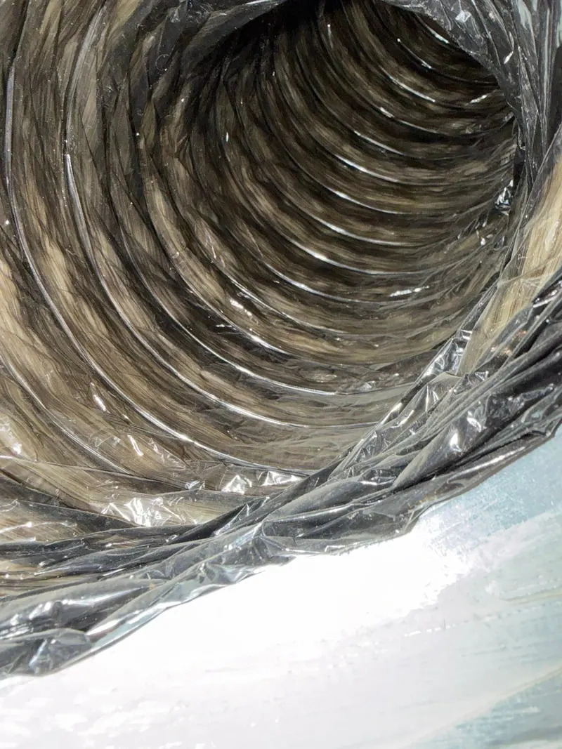 View down the inside of a flexible AC duct showing dust and debris on the inner liner