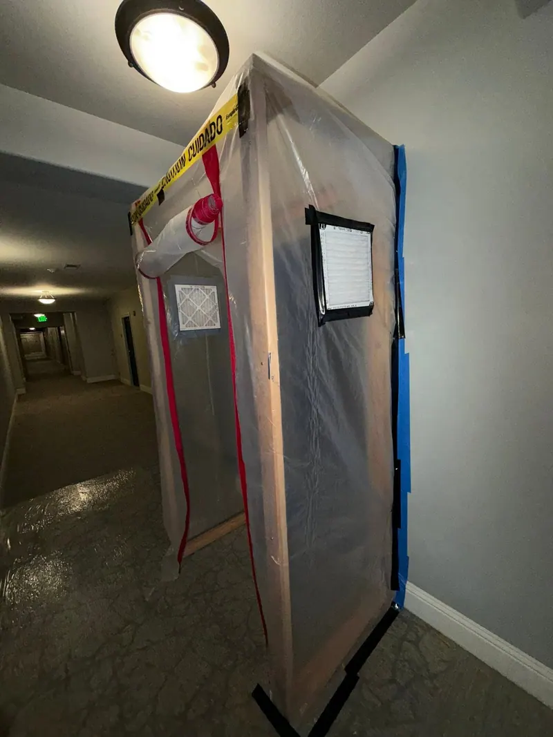 Floor-to-ceiling plastic containment with a zipper door and caution tape set up in a hallway